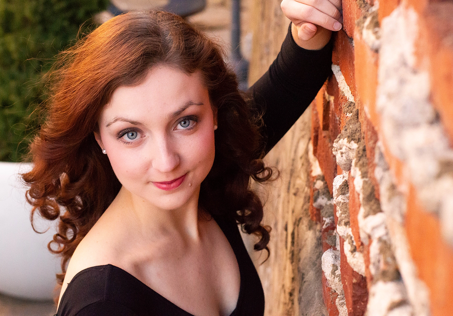 Close-up photo of an attractive young woman with red hair, green eyes, and fair skin leaning against a brick wall.