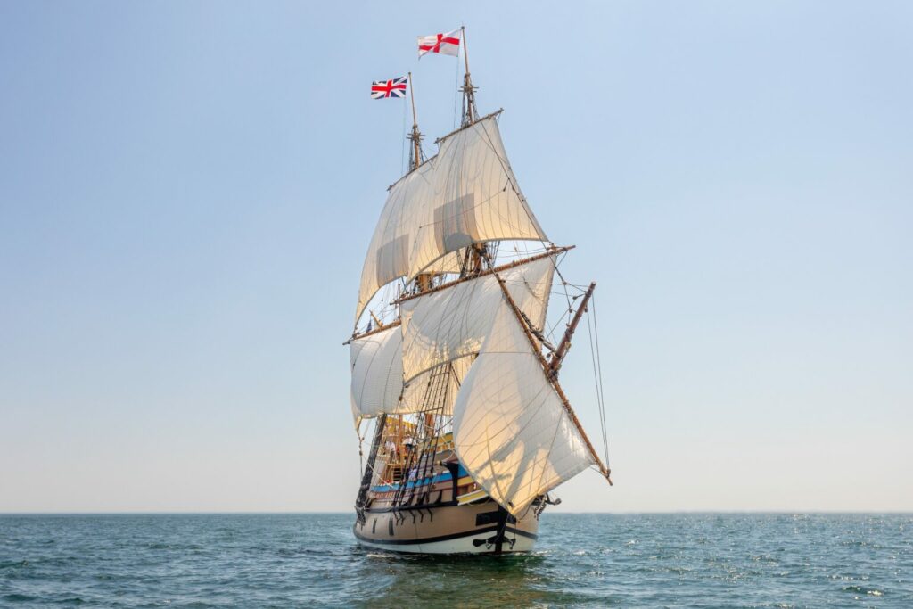 The Mayflower II, a replica of a ship from the 1600s, sails along the blue sea against a beautiful blue sky.